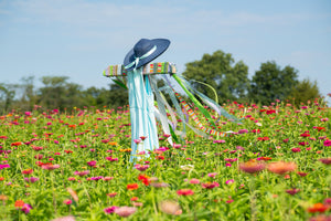 Decorative scarecrow with a hat and ribbons in a field of flowers under a clear blue sky.